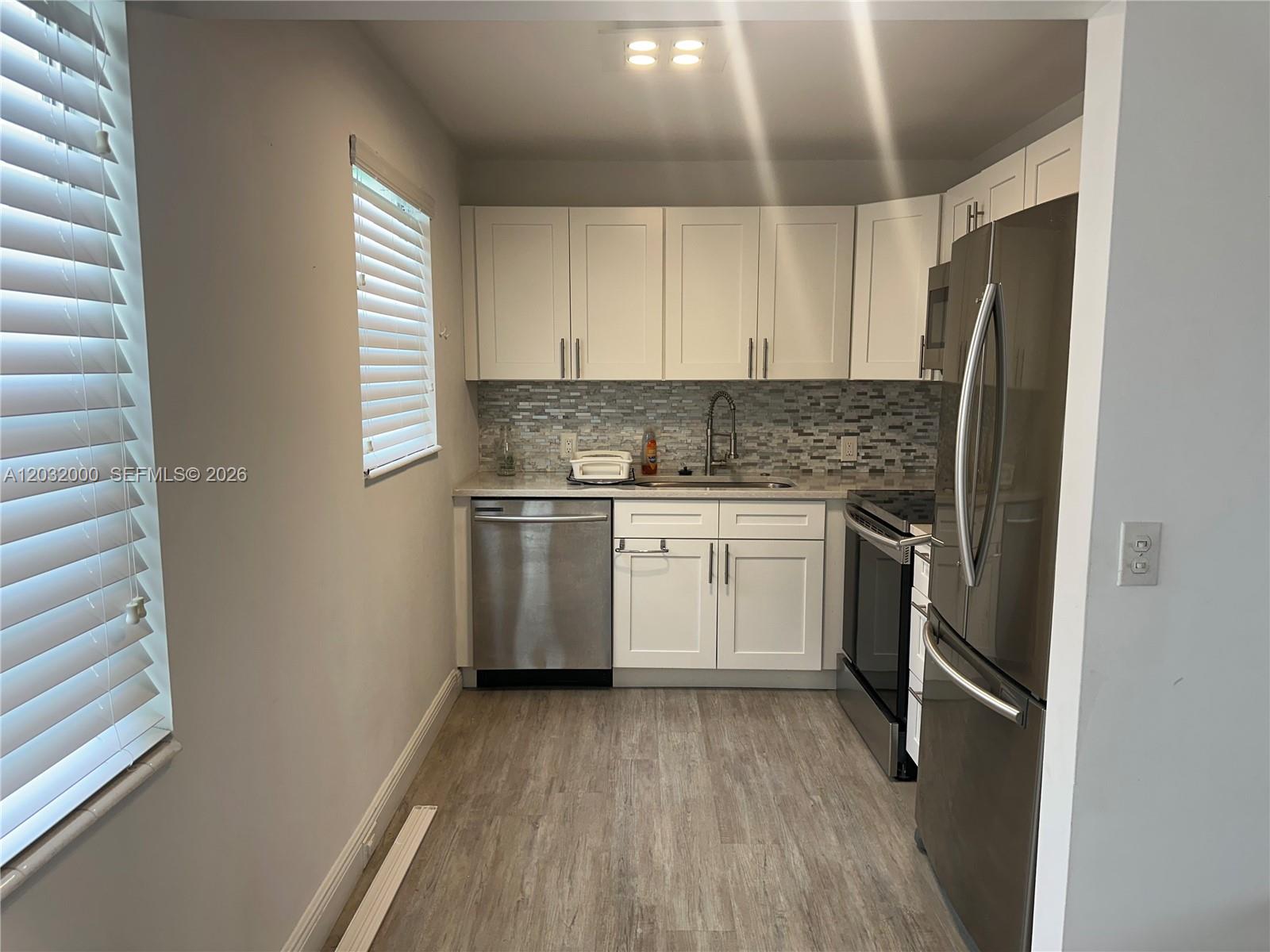 A galley kitchen features white cabinets, stainless steel appliances, and a mosaic tile backsplash — 445 Mansfield K # 445, Boca Raton FL 33434, BOCA RATON, FL