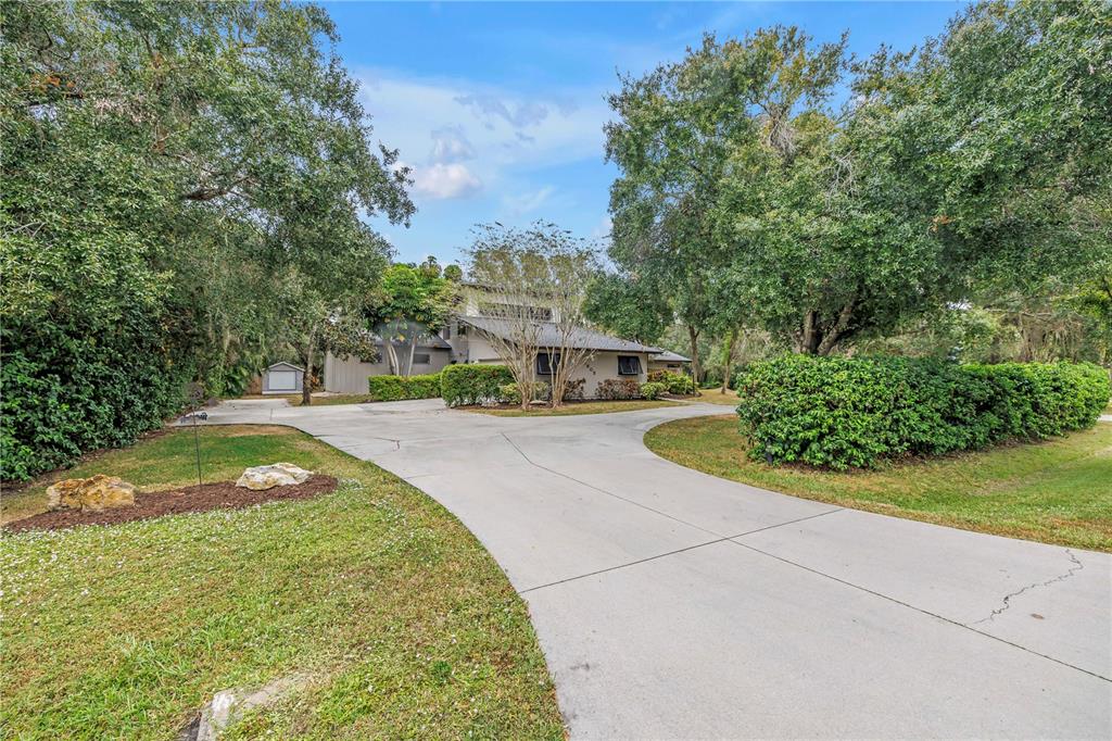 A concrete driveway leads to a two-story house surrounded by mature trees and landscaping — 4605 STONE RIDGE TRAIL, SARASOTA, FL
