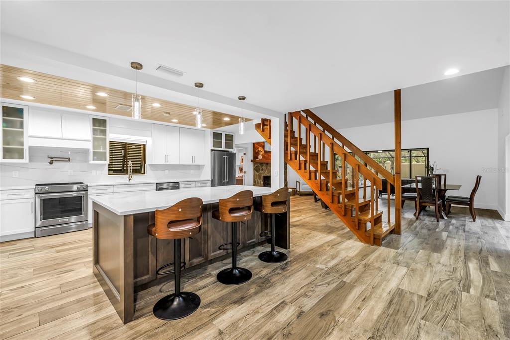 A kitchen with a center island and bar stools sits next to a wooden staircase — 4605 STONE RIDGE TRAIL, SARASOTA, FL