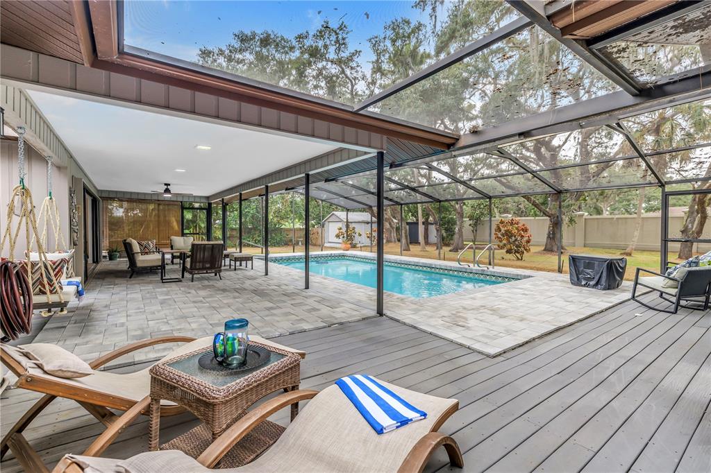 A screened-in patio features a swimming pool, paver deck, and wooden flooring with lounge seating — 4605 STONE RIDGE TRAIL, SARASOTA, FL