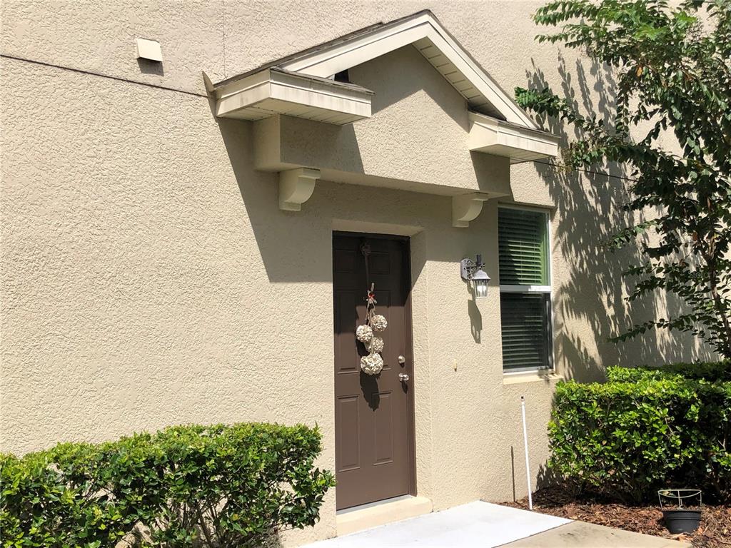 A brown front door sits beneath a small gabled roof overhang on a stucco building — 1548 PURPLE PLUM LANE, OVIEDO, FL