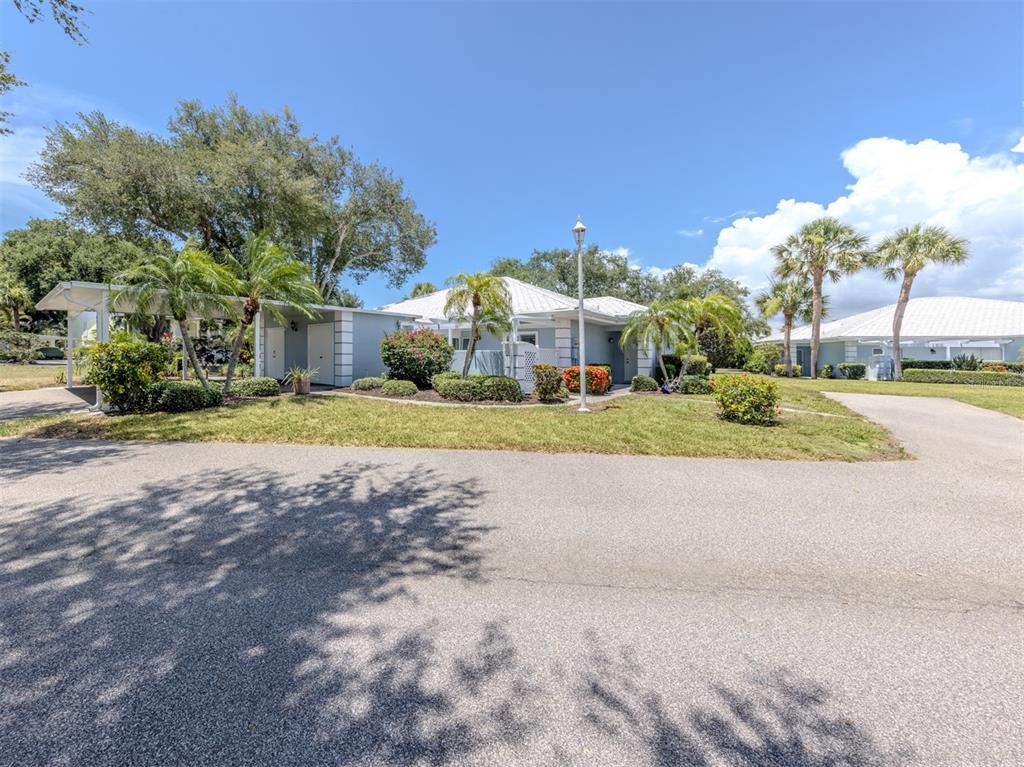 A single-story house with a carport and palm trees sits on a grassy lot — 431 WEXFORD CIRCLE UNIT 76, VENICE, FL