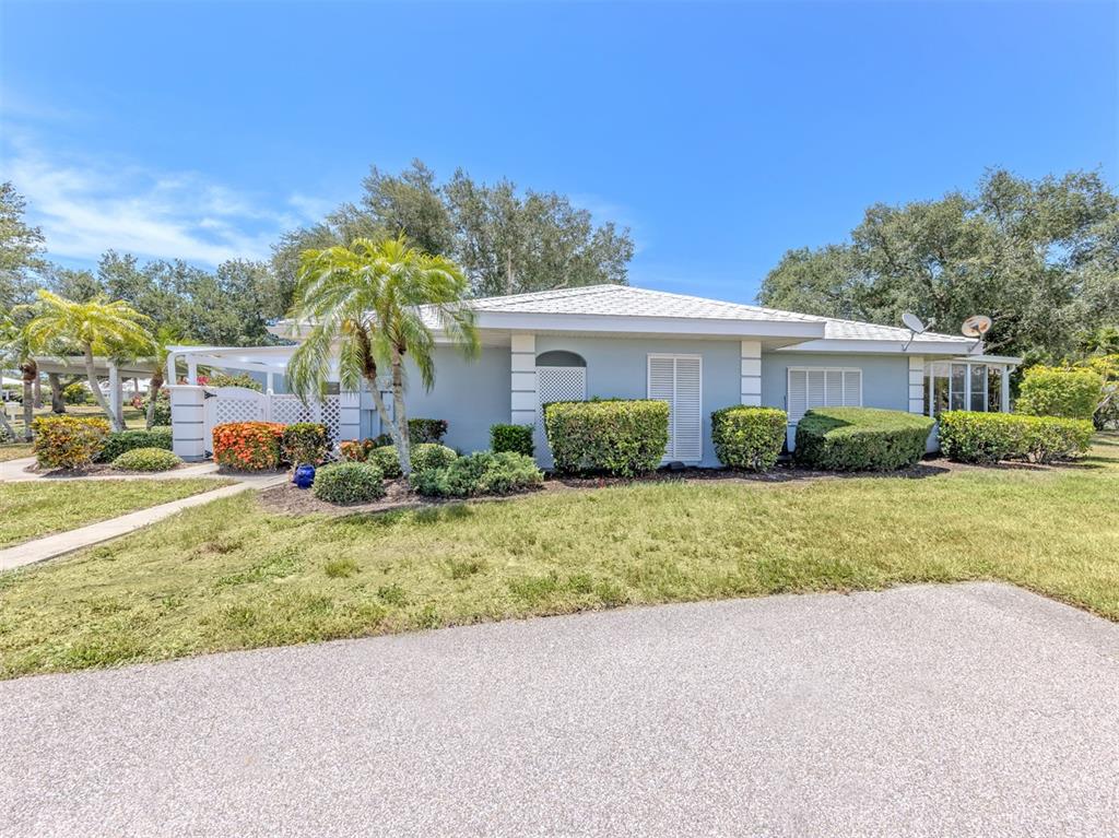 A light blue single-story house features a white roof, palm trees, and manicured landscaping — 431 WEXFORD CIRCLE UNIT 76, VENICE, FL