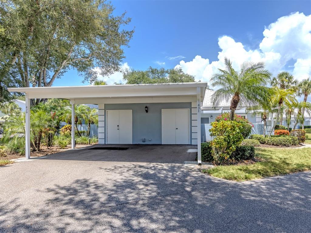 A carport with two white storage doors stands in front of a blue house — 431 WEXFORD CIRCLE UNIT 76, VENICE, FL