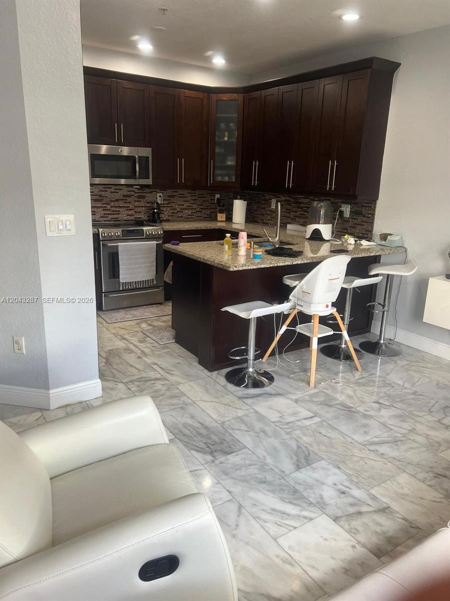A kitchen features dark wood cabinets, granite countertops, and light marble flooring — 4301 SW 160th Ave # 215, Miramar FL 33027, MIRAMAR, FL