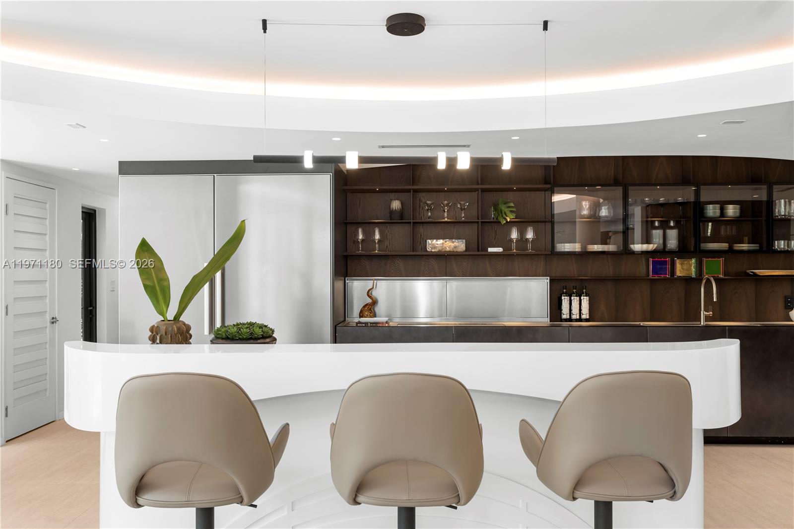 A modern kitchen features a curved white bar, three tan stools, and dark wood cabinetry — 5261 NE 5th Ave, Miami FL 33137, MIAMI, FL