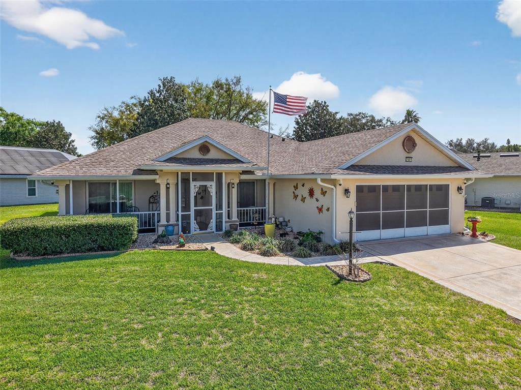 A single-story house with a tan exterior, a screened front porch, and a two-car garage — 21811 KING HENRY AVENUE, LEESBURG, FL