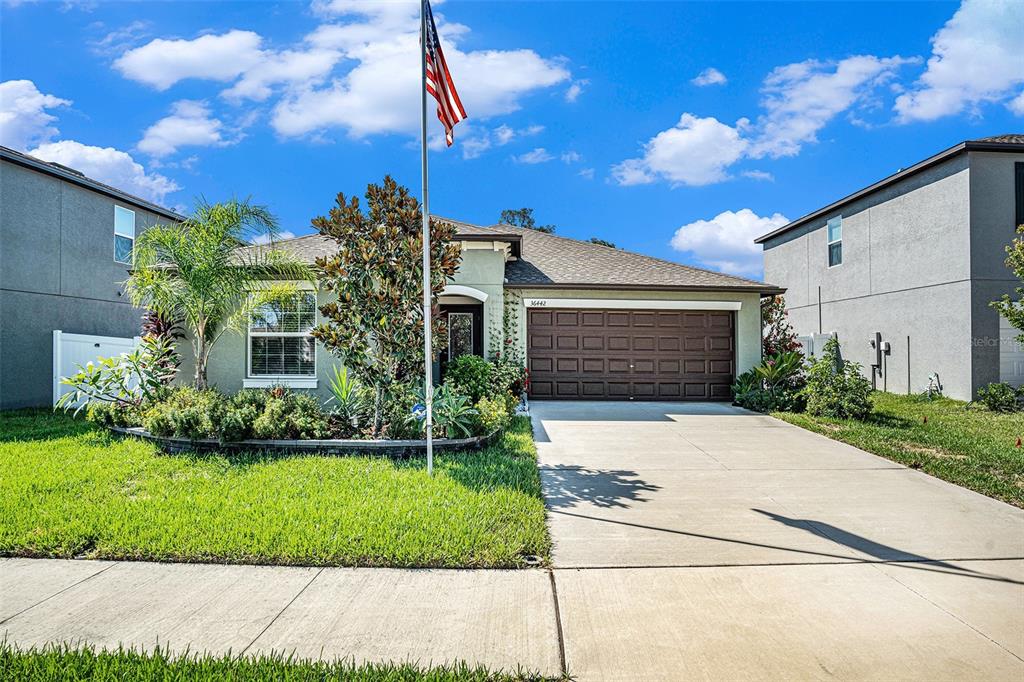 A single-story house with a brown garage door, a flag pole, and a landscaped yard — 36442 FLATS STREET, ZEPHYRHILLS, FL