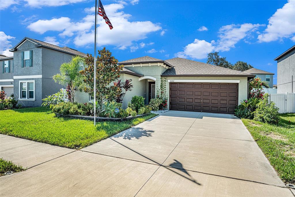 A single-story suburban house with a brown garage door, a driveway, and an American flag — 36442 FLATS STREET, ZEPHYRHILLS, FL
