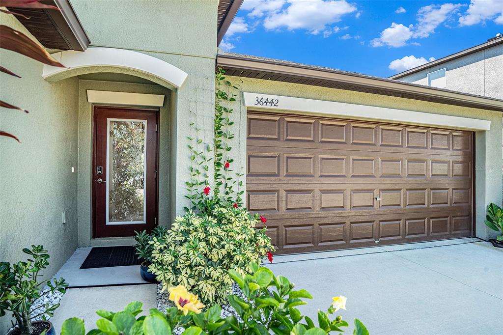 A front view of a house exterior featuring a brown garage door and entryway — 36442 FLATS STREET, ZEPHYRHILLS, FL
