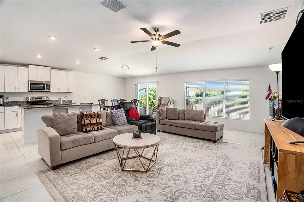 A living room with a sectional sofa, area rug, and an open kitchen with white cabinets — 36442 FLATS STREET, ZEPHYRHILLS, FL