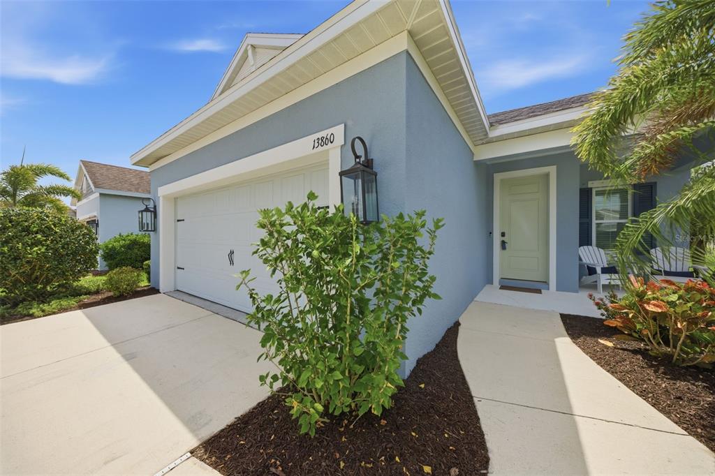 A light blue house exterior features a two-car garage, a front walkway, and landscaping — 13860 OLD CREEK COURT, PARRISH, FL
