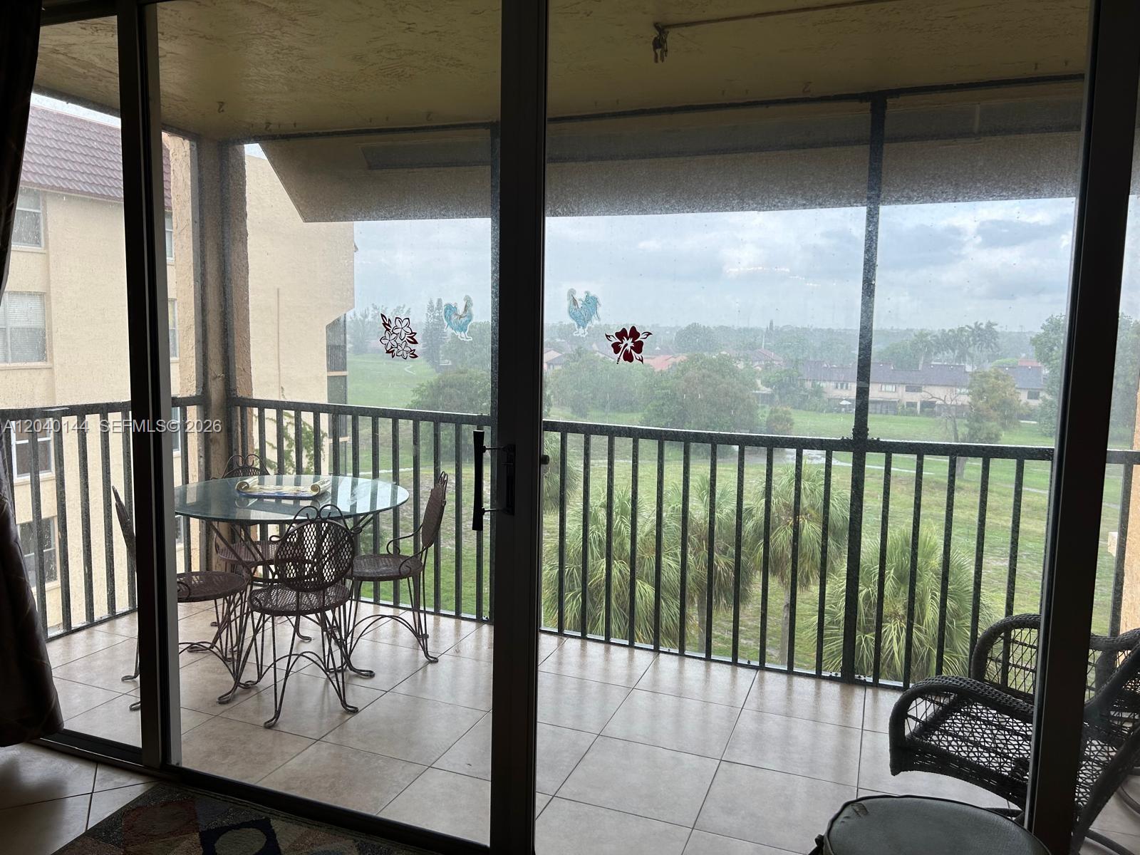 A tiled balcony with a glass table and chairs overlooks a grassy field and trees — 3841 Environ Blvd # 629, Lauderhill FL 33319, LAUDERHILL, FL