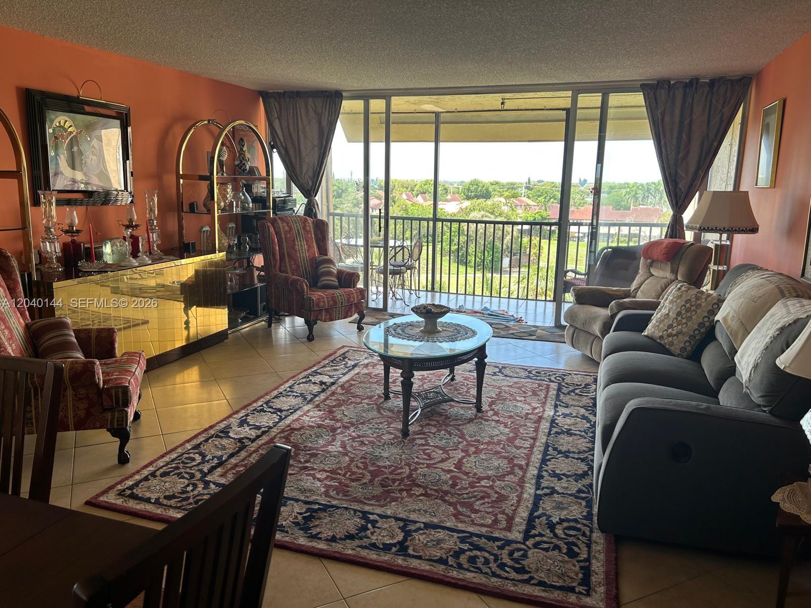 A living room features orange walls, a patterned area rug, and a balcony with views — 3841 Environ Blvd # 629, Lauderhill FL 33319, LAUDERHILL, FL