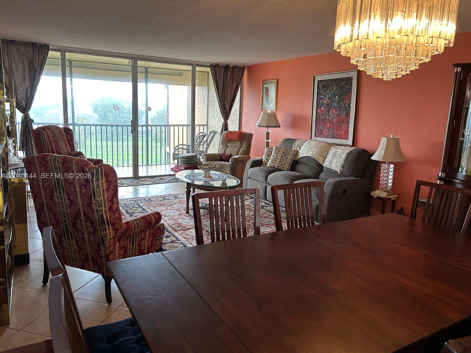 A living and dining area features coral walls, a crystal chandelier, and a balcony view — 3841 Environ Blvd # 629, Lauderhill FL 33319, LAUDERHILL, FL