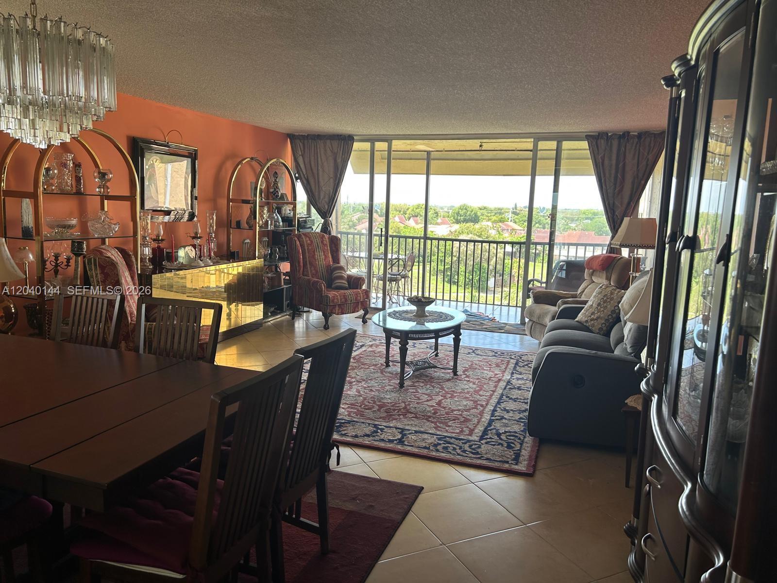 A living and dining room with orange walls, tile floors, and a balcony view — 3841 Environ Blvd # 629, Lauderhill FL 33319, LAUDERHILL, FL