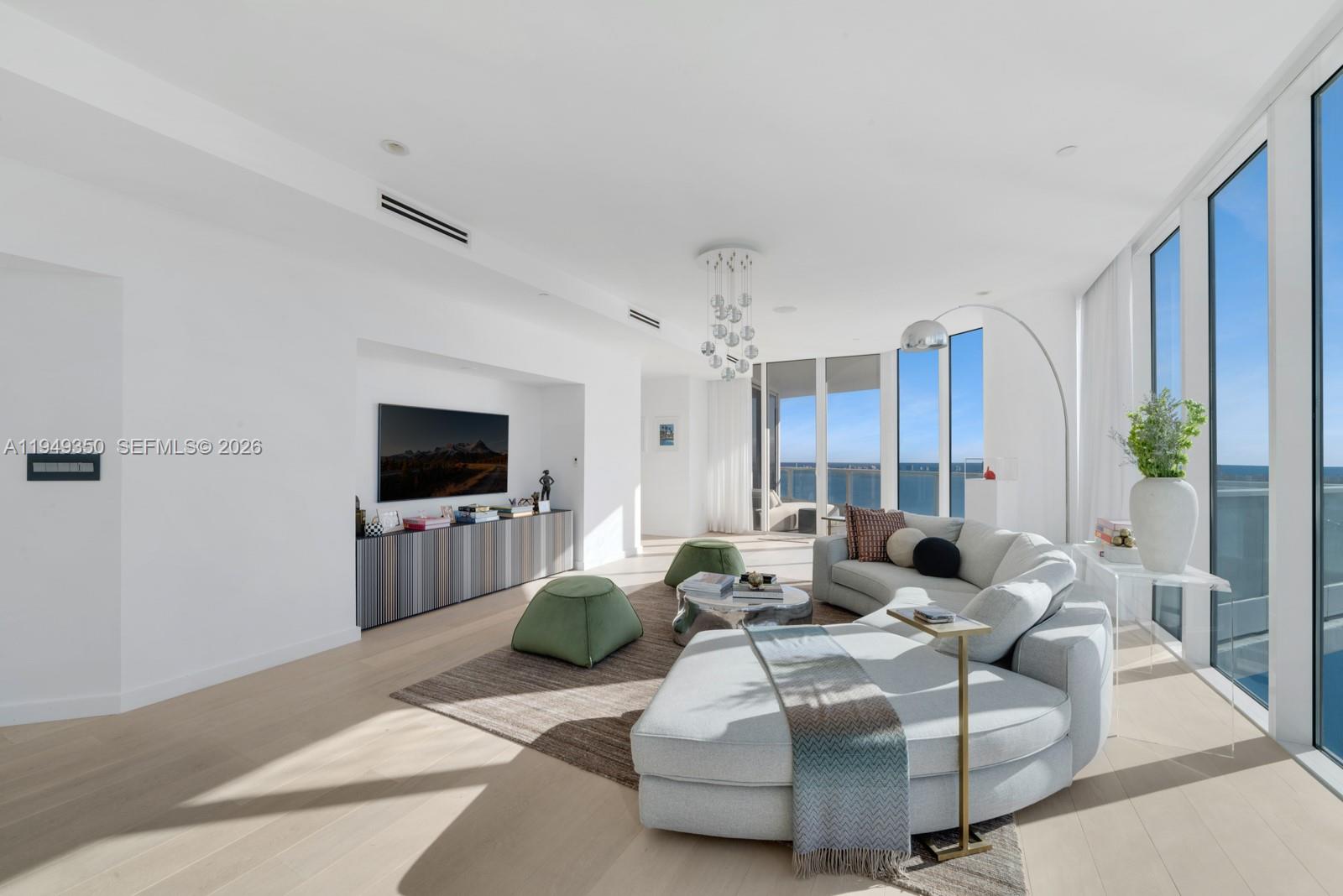 A bright living room features a curved sofa, green ottomans, and floor-to-ceiling ocean view windows — 2020 N Bayshore Dr, Miami FL 33137, MIAMI, FL