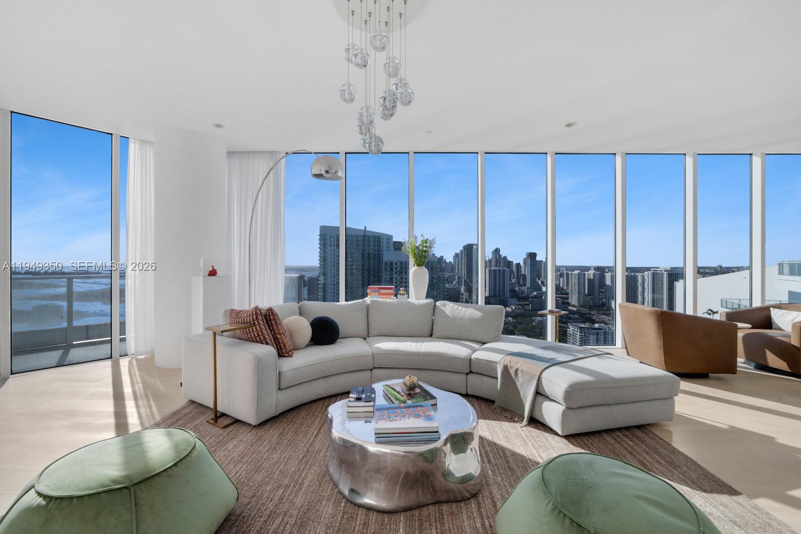 A modern living room features a curved sofa, metallic coffee table, and floor-to-ceiling city views — 2020 N Bayshore Dr, Miami FL 33137, MIAMI, FL