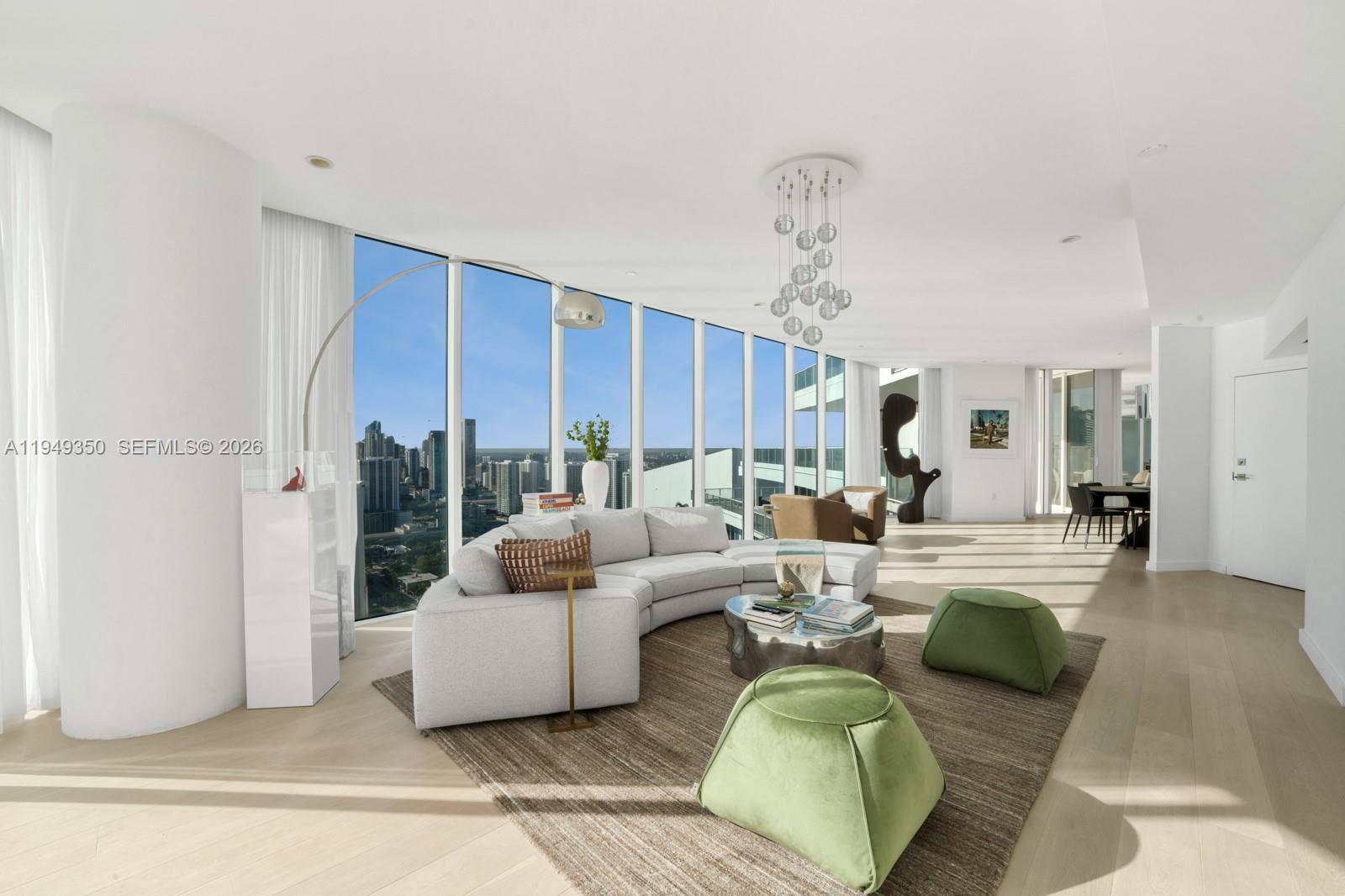 A modern living room features a curved sofa, green ottomans, and floor-to-ceiling city views — 2020 N Bayshore Dr, Miami FL 33137, MIAMI, FL