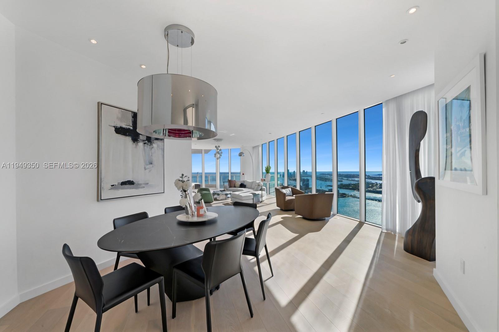 A modern dining area with a dark oval table overlooks a coastal city view — 2020 N Bayshore Dr, Miami FL 33137, MIAMI, FL