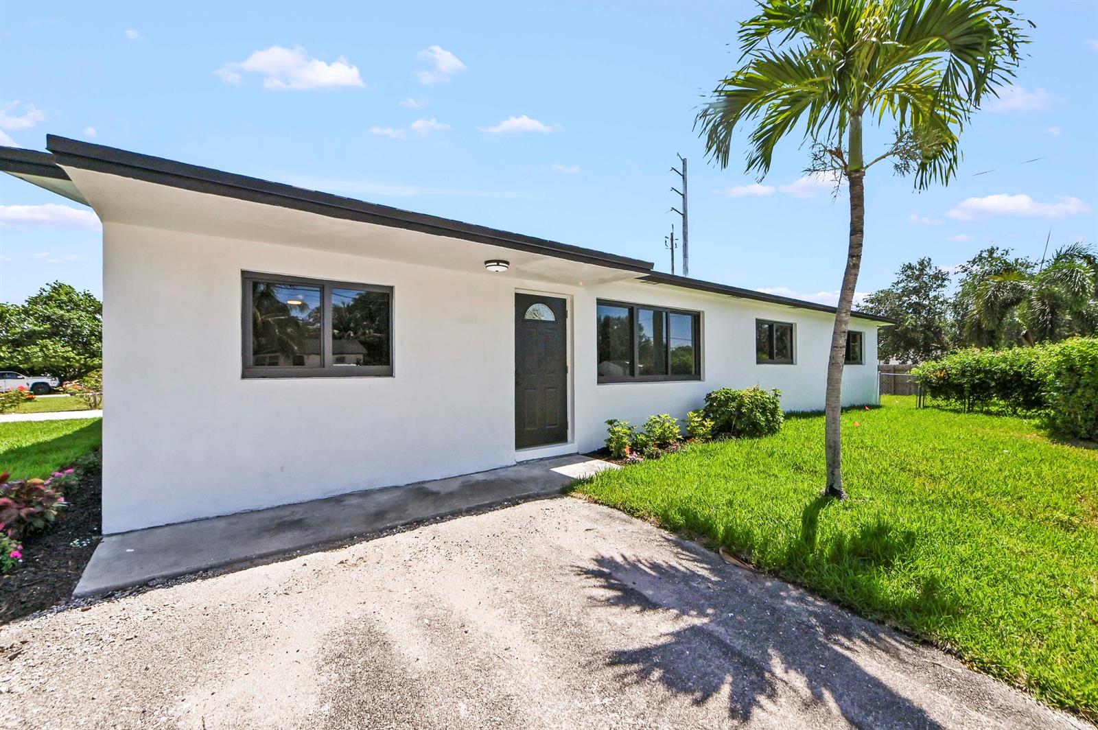 A white, single-story house with a dark front door and a palm tree in front — 3645 Melaleuca Lane, Lake Worth FL 33461, LAKE WORTH, FL