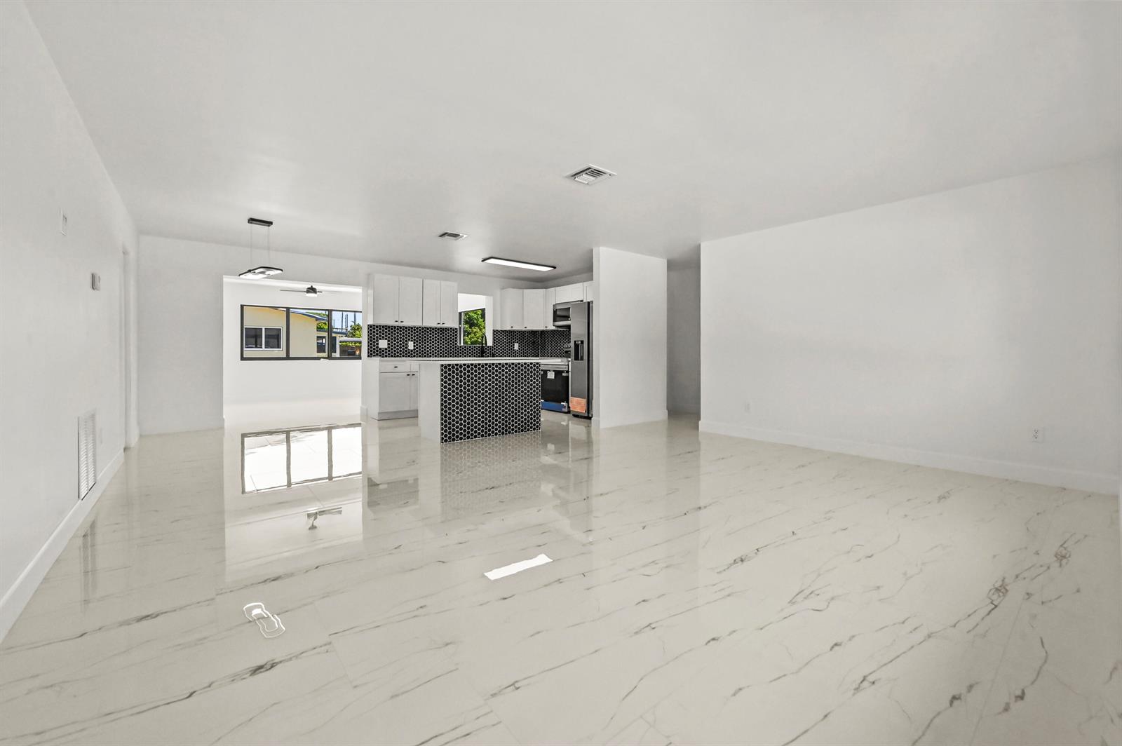 An open-concept living area features white marble-look tile flooring and a kitchen with black tiling — 3645 Melaleuca Lane, Lake Worth FL 33461, LAKE WORTH, FL