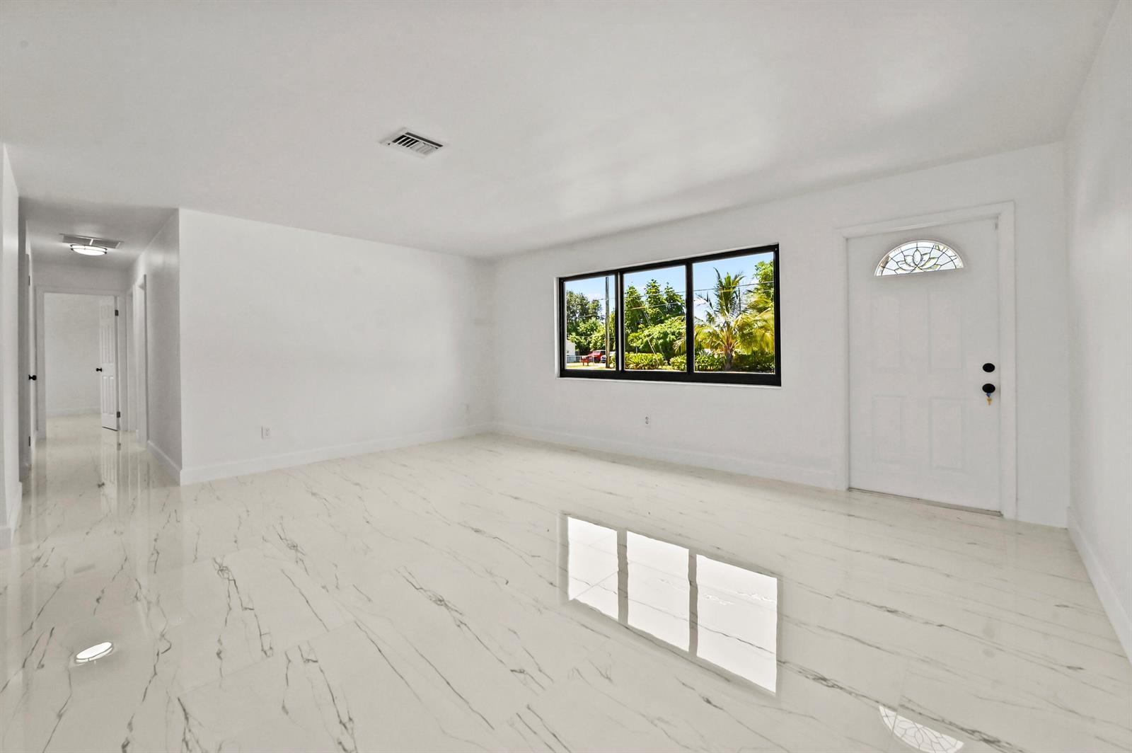 A bright, empty living room features white walls, marble-look tile flooring, and a front door — 3645 Melaleuca Lane, Lake Worth FL 33461, LAKE WORTH, FL