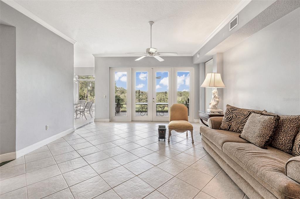 A living room features light tile flooring, a tan sofa, a ceiling fan, and glass doors — 901 CAMINO REAL BOULEVARD UNIT 901, HOWEY IN THE HILLS, FL