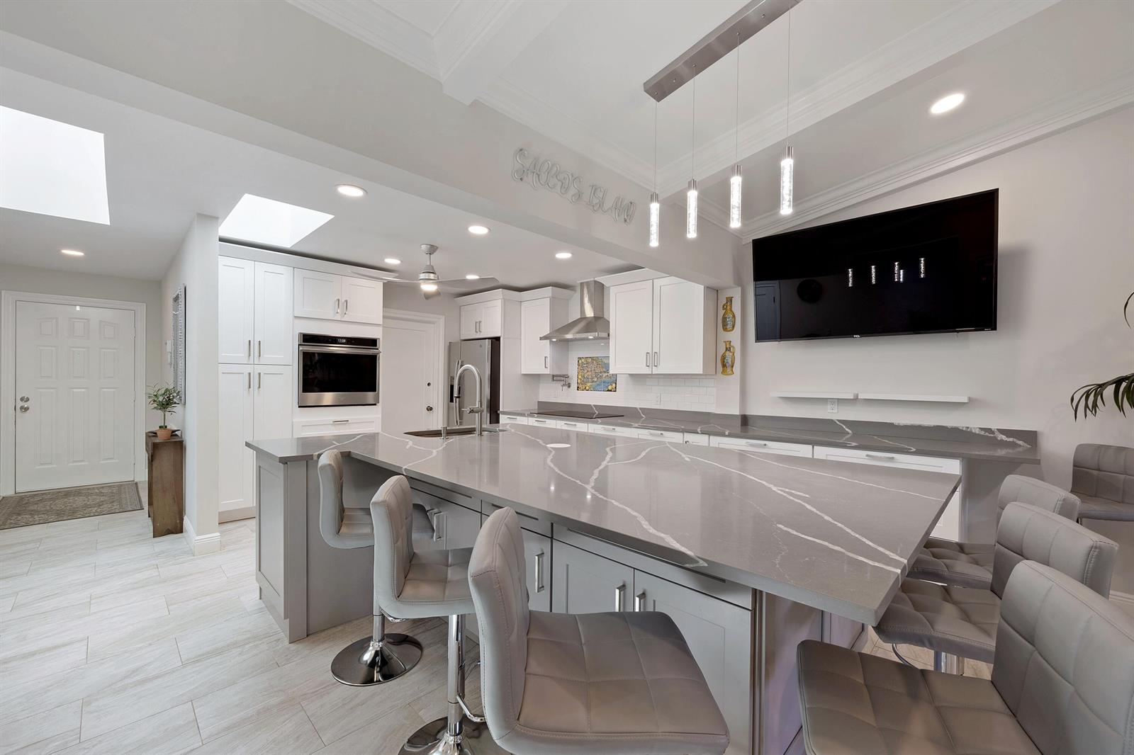A modern kitchen features a large gray quartz island, white cabinetry, and gray bar stools — 7 Ridge Pointe Drive # C, Boynton Beach FL 33435, BOYNTON BEACH, FL