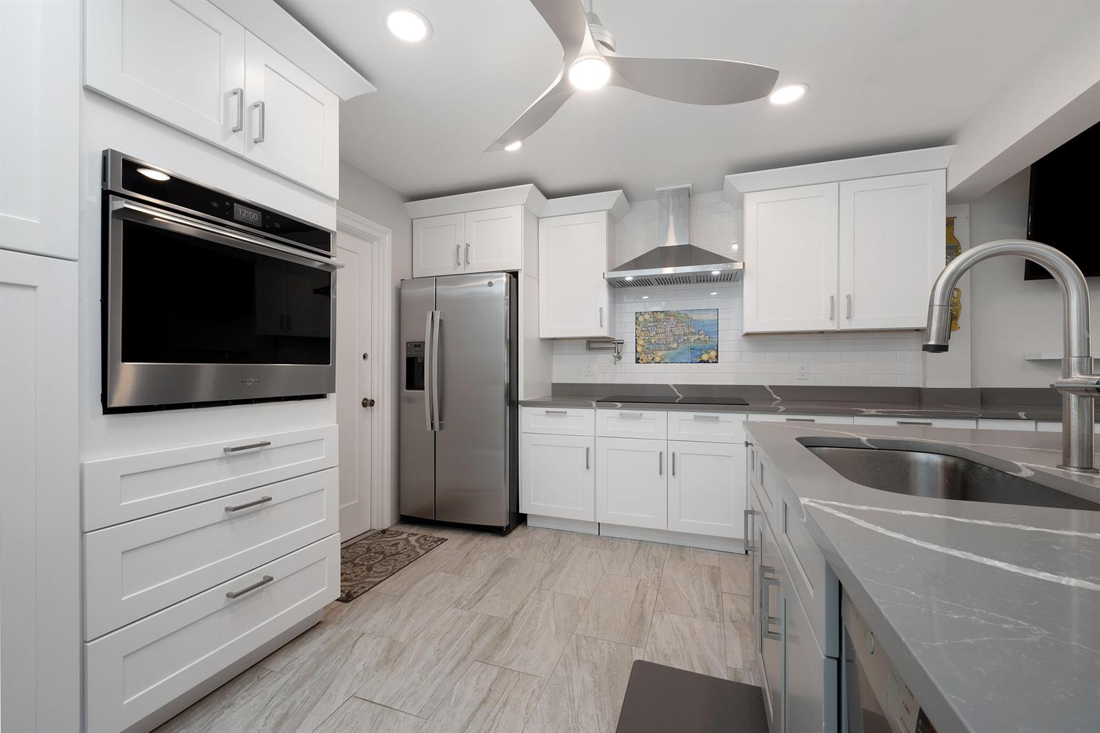 A modern kitchen features white cabinetry, stainless steel appliances, and gray quartz countertops — 7 Ridge Pointe Drive # C, Boynton Beach FL 33435, BOYNTON BEACH, FL