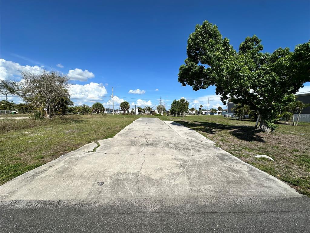A concrete driveway leads into a vacant, grassy lot under a clear blue sky — 1427 SEAGULL DRIVE, ENGLEWOOD, FL