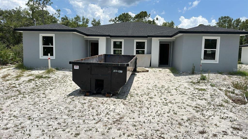 A newly constructed gray house with a black roof and a large dumpster in front — 17099 CARLEEN AVENUE, PORT CHARLOTTE, FL