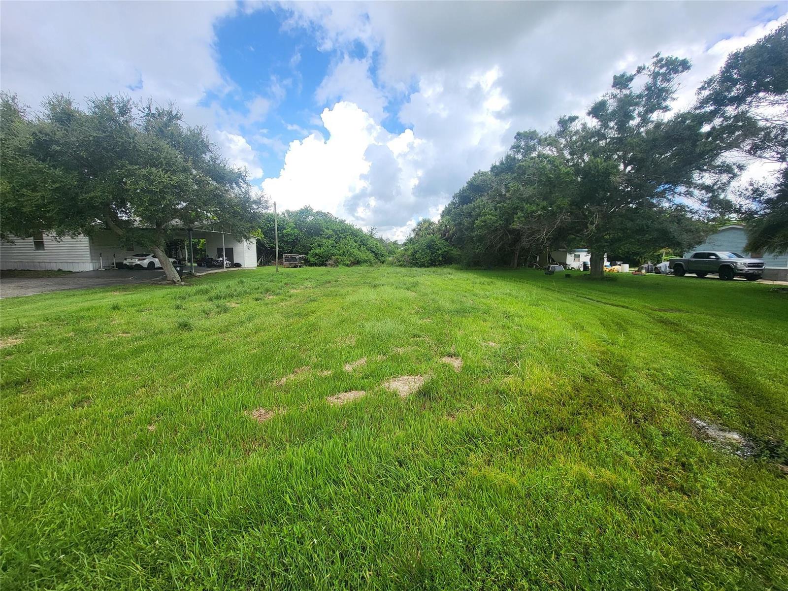 A grassy vacant lot sits between two residential properties under a cloudy blue sky — 1099 Pine Avenue, Moore Haven FL 33471, MOORE HAVEN, FL