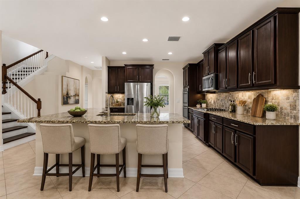 A kitchen features dark wood cabinets, granite countertops, a central island, and three bar stools — 4424 VERMILLION SKY DRIVE, WESLEY CHAPEL, FL