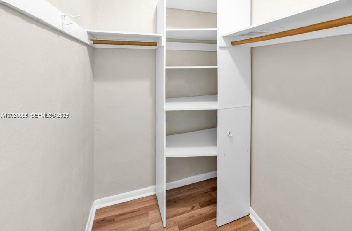 A walk-in closet features white shelving units, hanging rods, and wood-look flooring — 18801 NE 2nd Ave # 1006, Miami FL 33179, MIAMI, FL