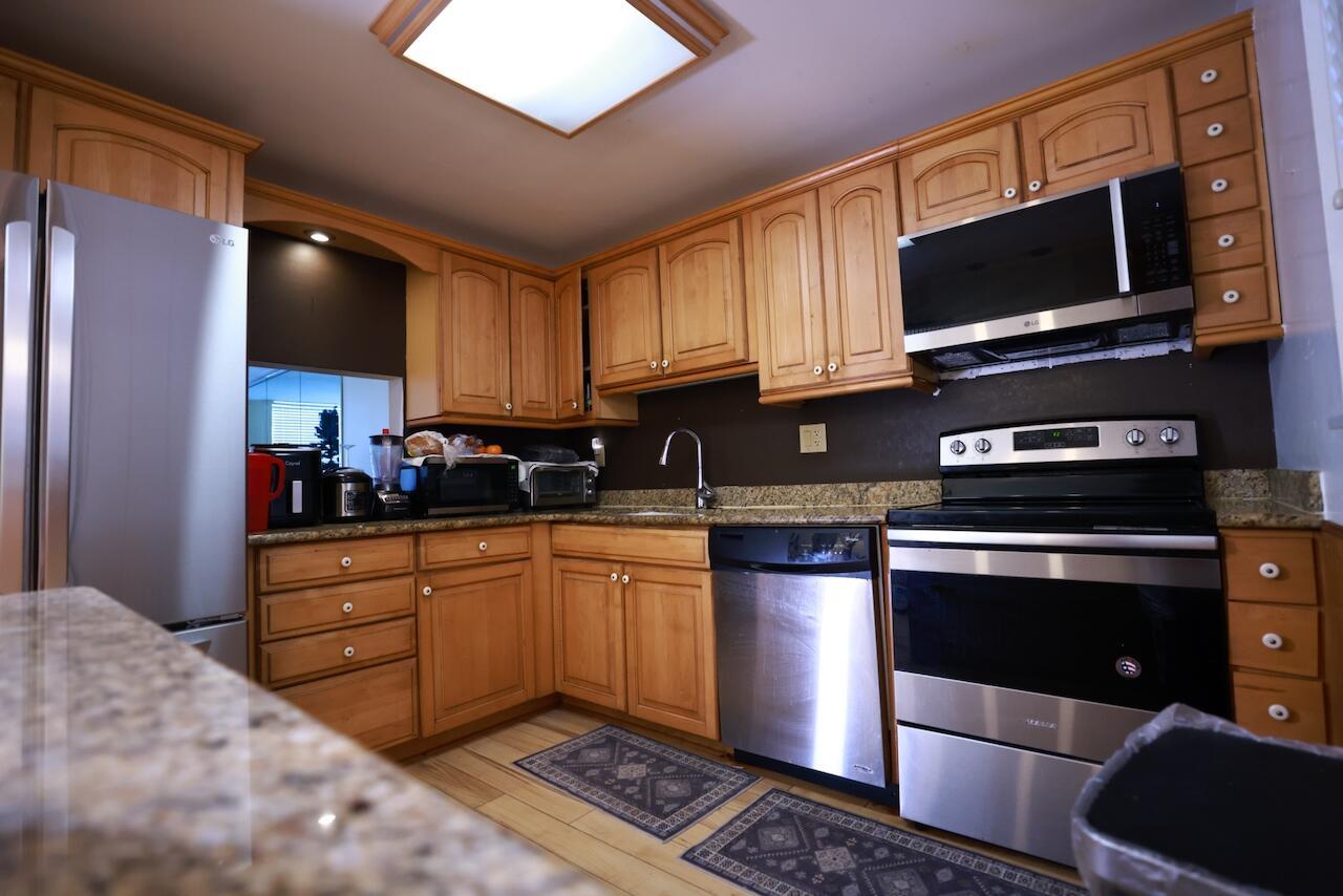 A kitchen with wood cabinets, stainless steel appliances, granite countertops, and a dark backsplash — 6570 Royal Palm Boulevard # 106j, Margate FL 33063, MARGATE, FL