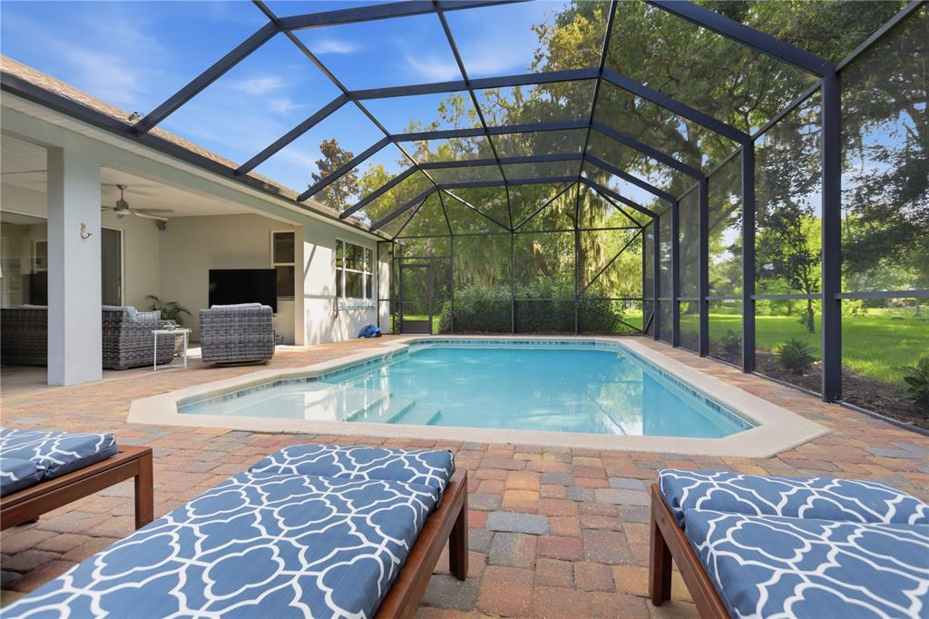 A screened-in patio features a rectangular swimming pool, brick pavers, and outdoor lounge furniture — 108 SUFFOLK CT., DELAND, FL