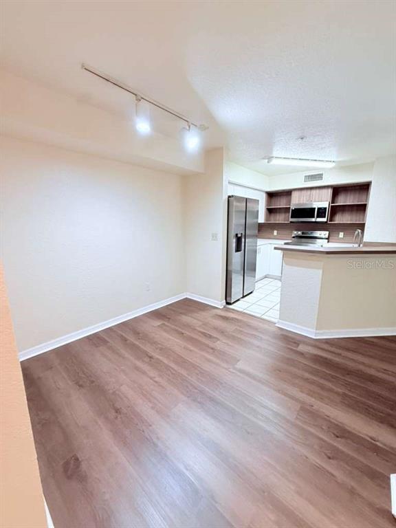 This room features wood-look flooring, a track lighting fixture, and an open kitchen area — 832 CAMARGO WAY UNIT 105, ALTAMONTE SPRINGS, FL