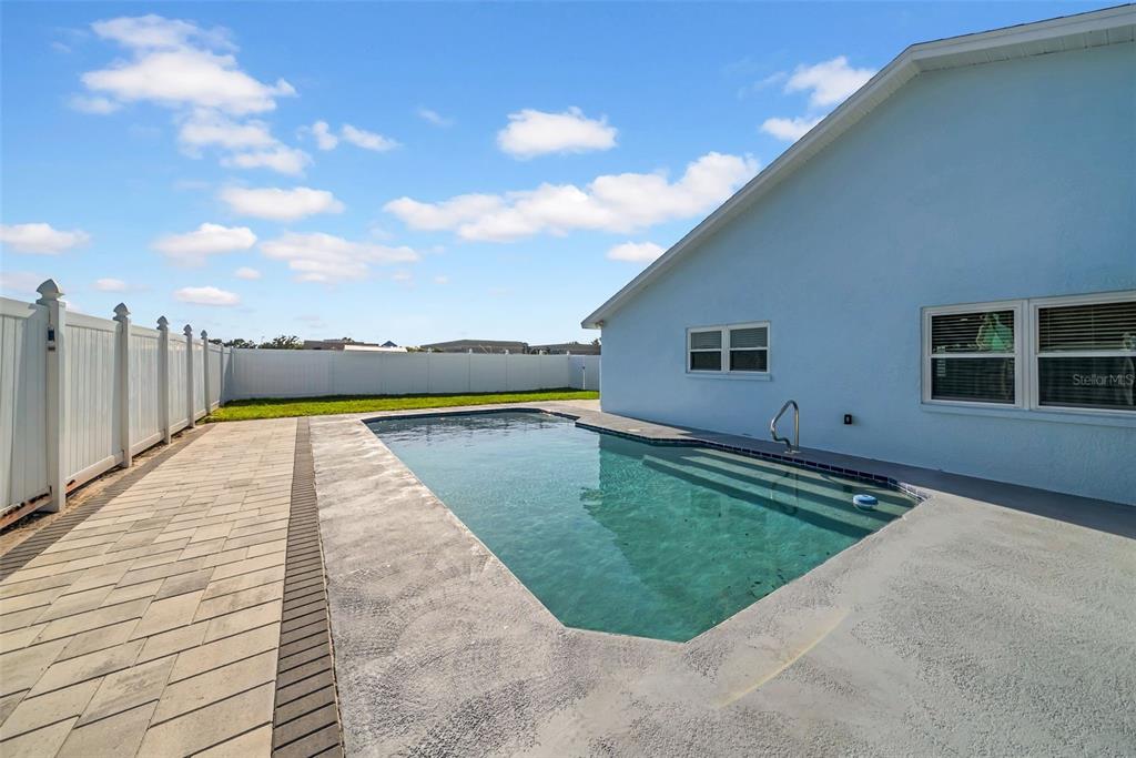 A rectangular swimming pool sits beside a light blue house with a white vinyl fence — 2020 58TH AVENUE S, ST PETERSBURG, FL