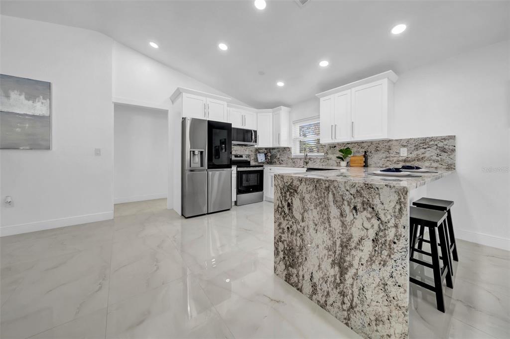 A modern kitchen features white cabinets, granite countertops, and a large island with bar stools — 2020 58TH AVENUE S, ST PETERSBURG, FL