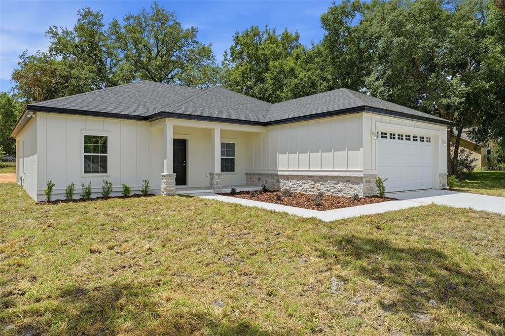 A single-story house with white board-and-batten siding, stone accents, and a two-car garage — 13404 NEW YORK AVENUE, ASTATULA, FL