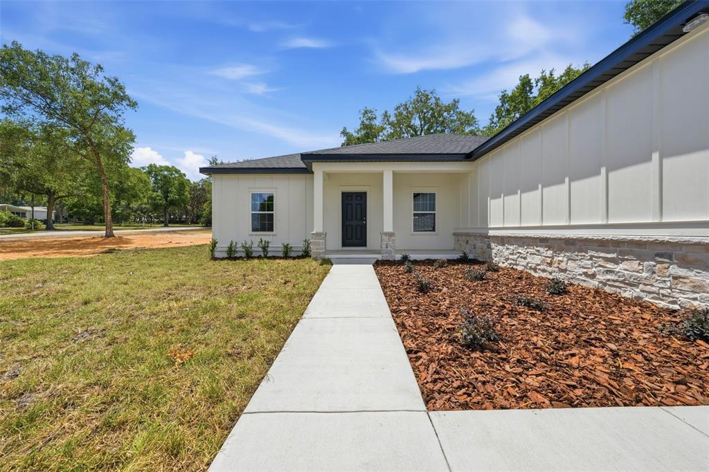 A white house with board-and-batten siding, stone accents, and a concrete walkway to the entrance — 13404 NEW YORK AVENUE, ASTATULA, FL