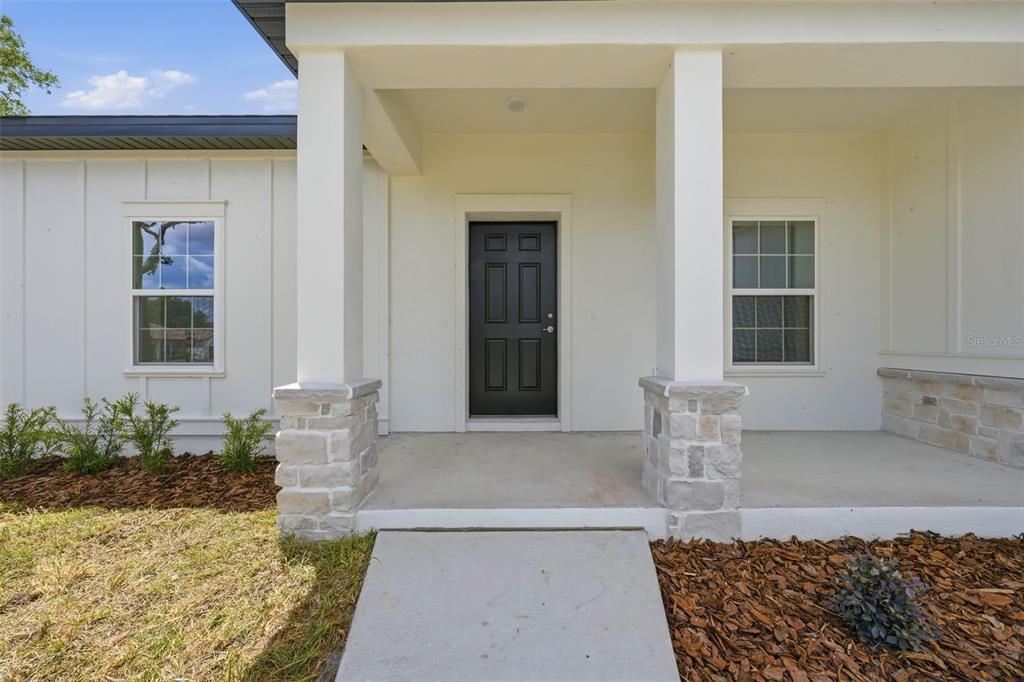 A white house exterior features a black front door, stone-based columns, and a concrete porch — 13404 NEW YORK AVENUE, ASTATULA, FL