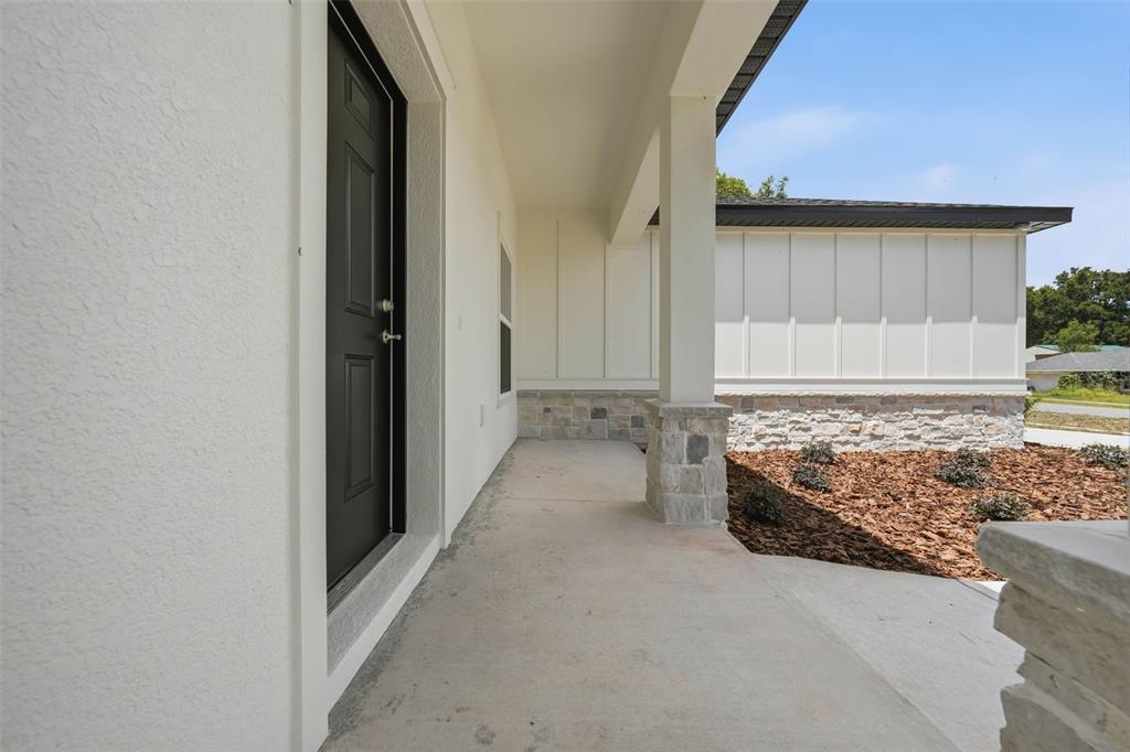 A covered concrete porch features a black front door and stone-accented support columns — 13404 NEW YORK AVENUE, ASTATULA, FL