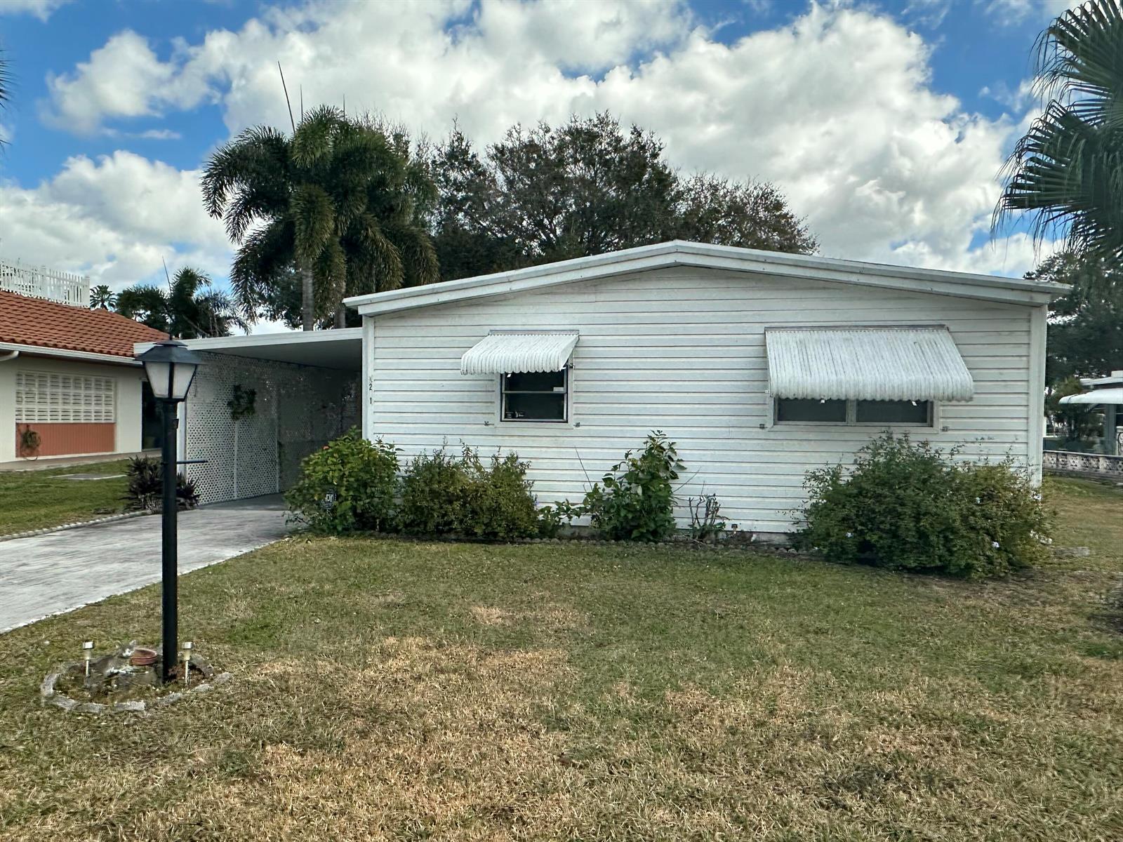 A white single-story mobile home features a carport, metal window awnings, and a front lawn — 8261 E Club Road, Boca Raton FL 33433, BOCA RATON, FL
