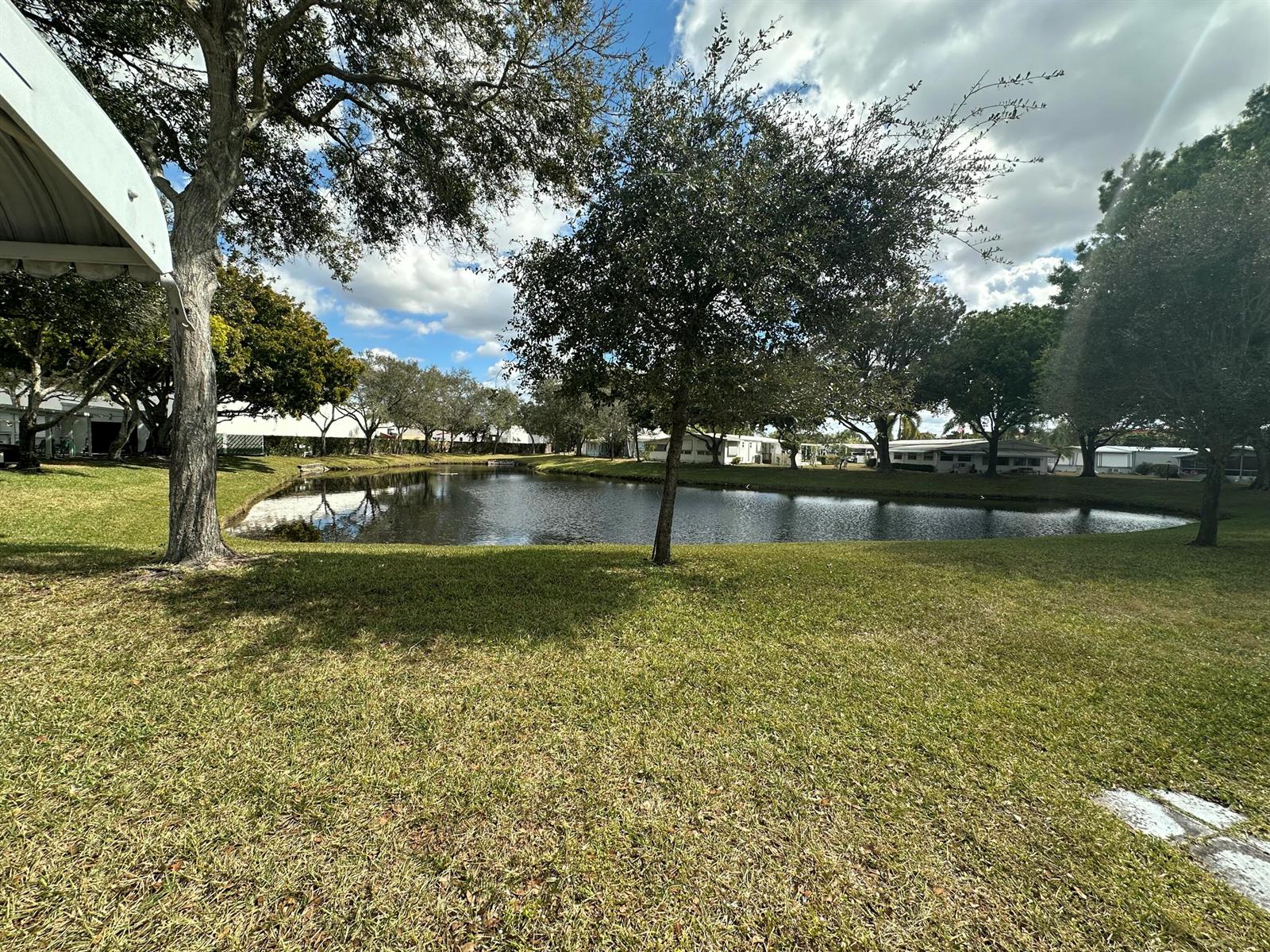 A grassy lawn leads to a small pond surrounded by trees and residential buildings — 8261 E Club Road, Boca Raton FL 33433, BOCA RATON, FL