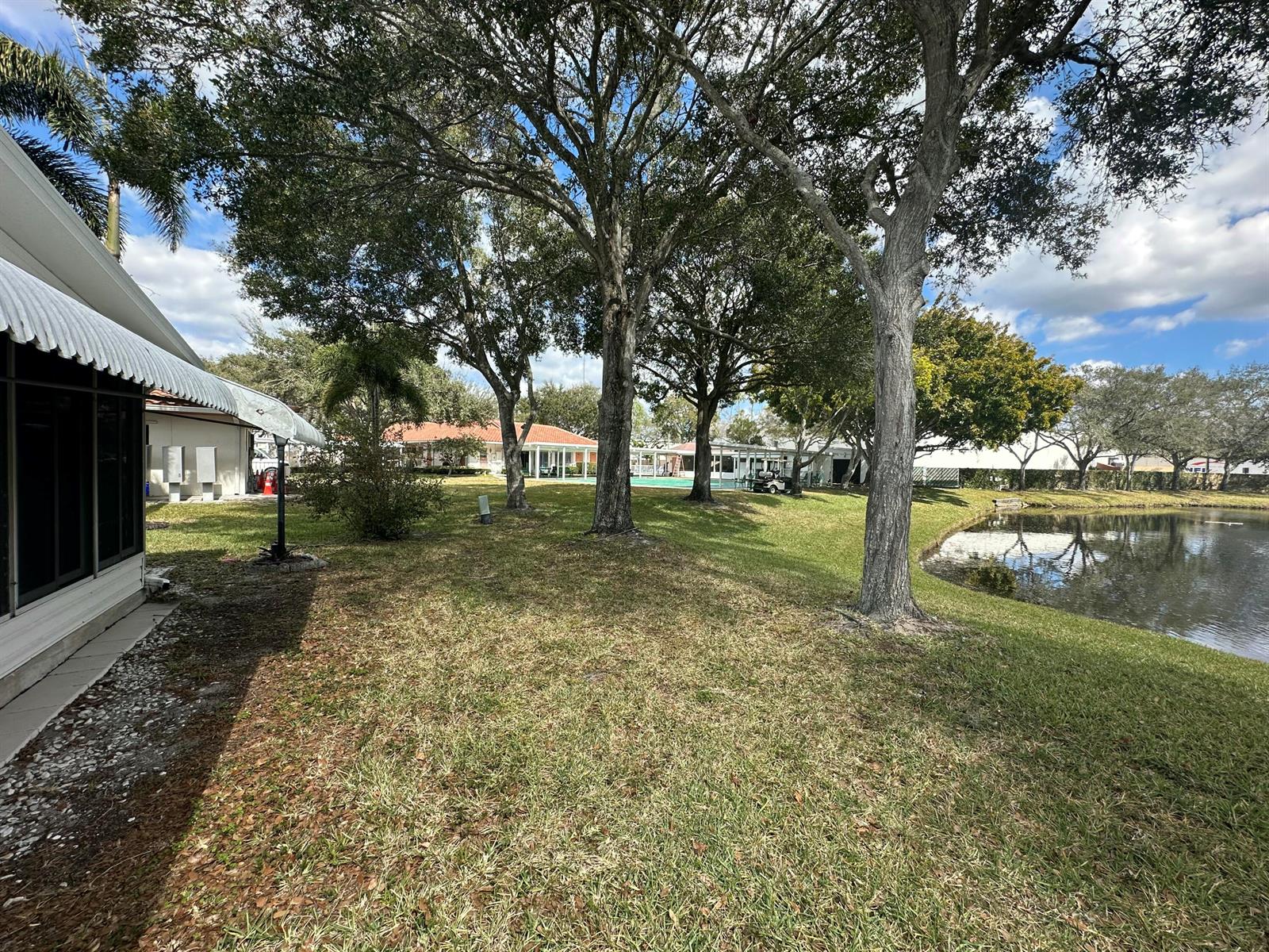 A grassy backyard features mature trees, a small pond, and a view of neighboring homes — 8261 E Club Road, Boca Raton FL 33433, BOCA RATON, FL