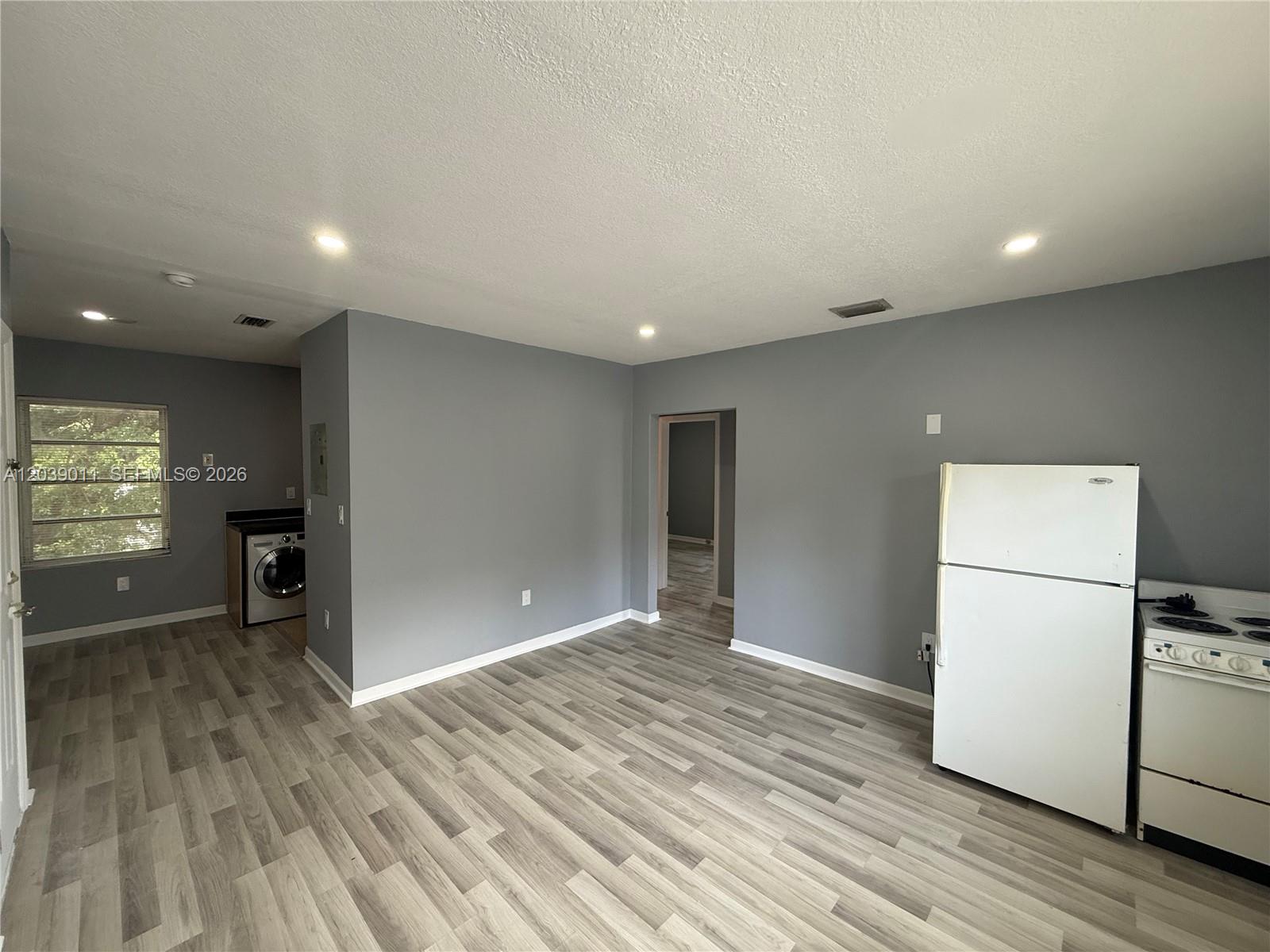 This kitchen and living area features gray walls, wood-look flooring, and a white refrigerator — 426 NE 77th St Rd # 4, Miami FL 33138, MIAMI, FL