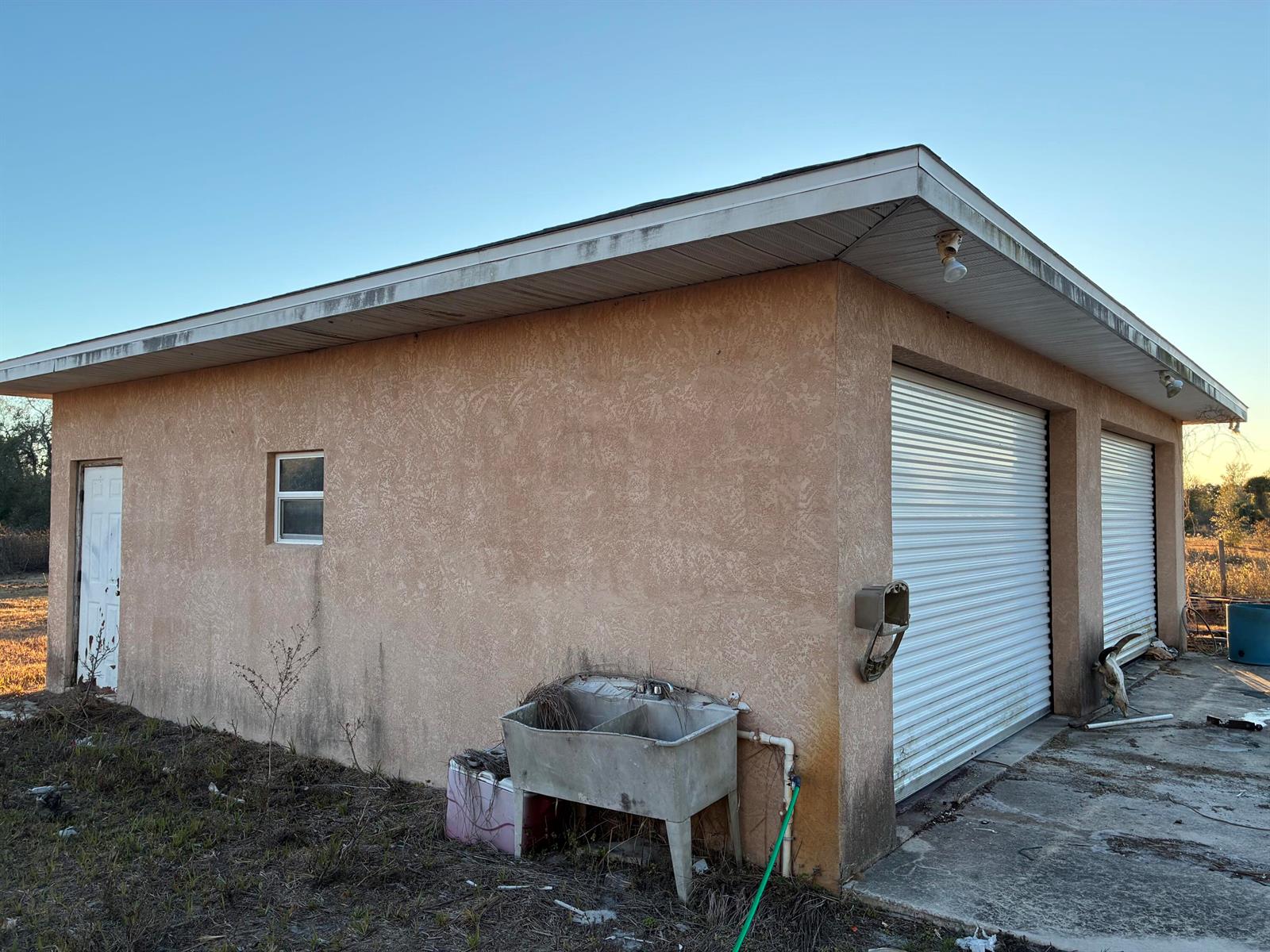 A tan stucco detached garage with two roll-up doors, a side door, and an exterior sink — 18034 NW 286th Street, Okeechobee FL 34972, OKEECHOBEE, FL
