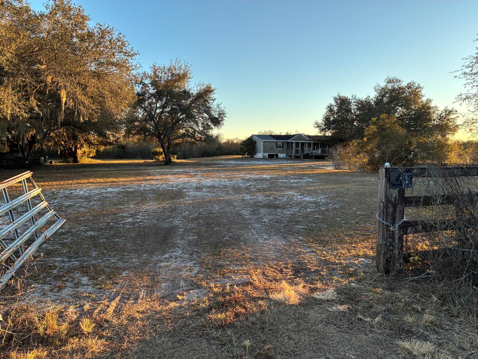A wide, sandy yard leads to a single-story home behind a gated wooden fence — 18034 NW 286th Street, Okeechobee FL 34972, OKEECHOBEE, FL